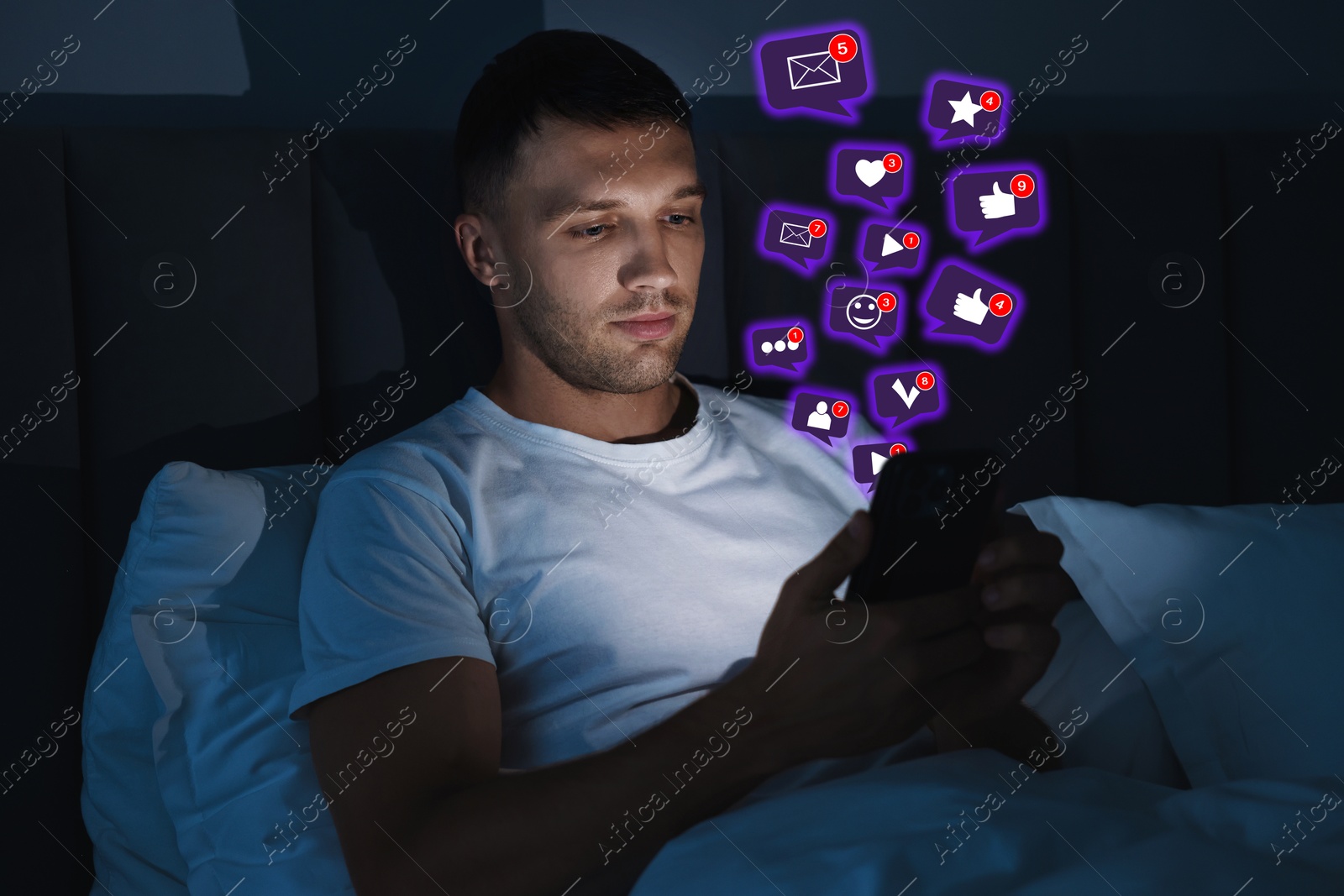 Image of Man using mobile phone in bed at night. New message sign and other notifications over gadget