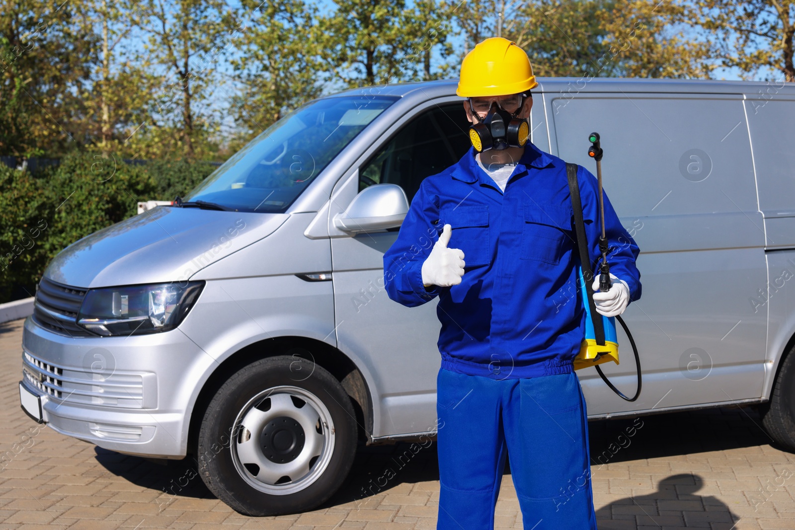 Photo of Pest control worker with spray tank showing thumbs up outdoors