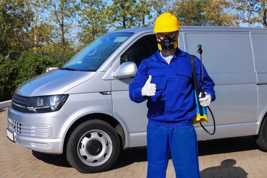 Photo of Pest control worker with spray tank showing thumbs up outdoors