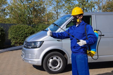 Photo of Pest control worker with spray tank showing thumbs up outdoors