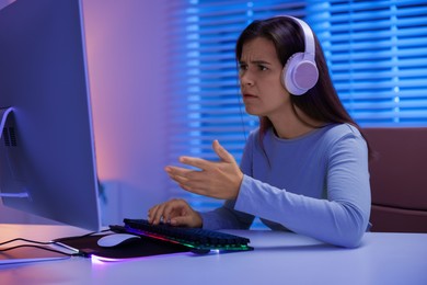 Photo of Emotional woman in headphones playing video game with keyboard at table indoors