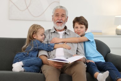 Grandpa and his grandkids reading book together on sofa at home