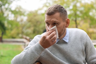 Man with tissue blowing runny nose in park