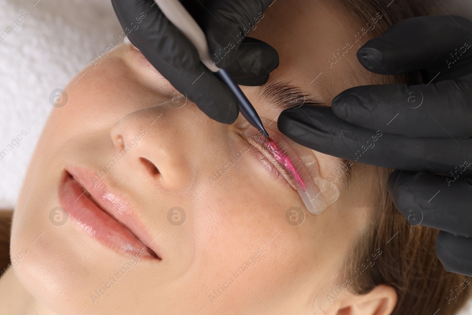 Photo of Eyelash lamination procedure. Esthetician applying lotion on woman's lashes in beauty salon, closeup