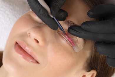 Photo of Eyelash lamination procedure. Esthetician applying lotion on woman's lashes in beauty salon, closeup