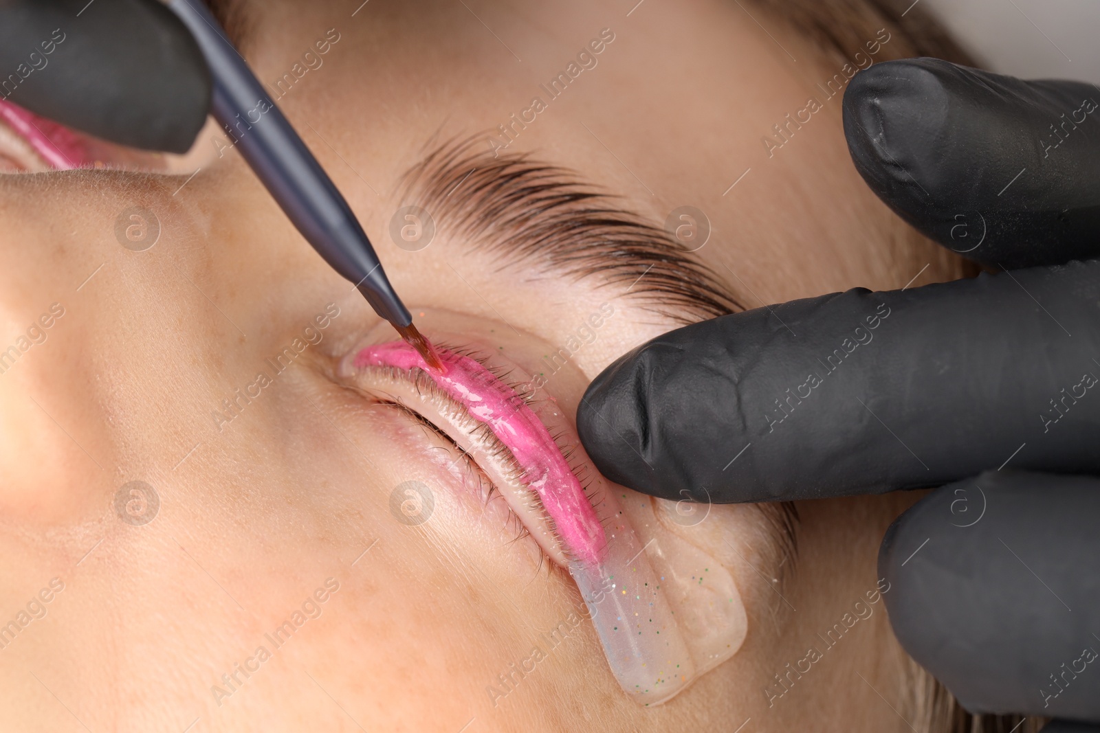 Photo of Eyelash lamination procedure. Esthetician applying lotion on woman's lashes in beauty salon, closeup