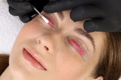 Photo of Eyelash lamination procedure. Esthetician wiping lotion from woman's lashes in beauty salon, closeup