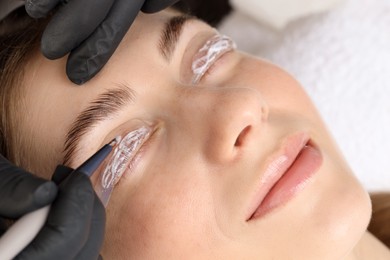 Photo of Eyelash lamination procedure. Esthetician applying lotion on woman's lashes in beauty salon, closeup