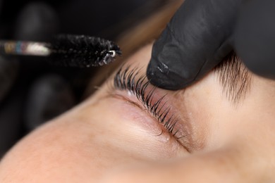 Photo of Esthetician brushing woman's lashes after lamination procedure, closeup