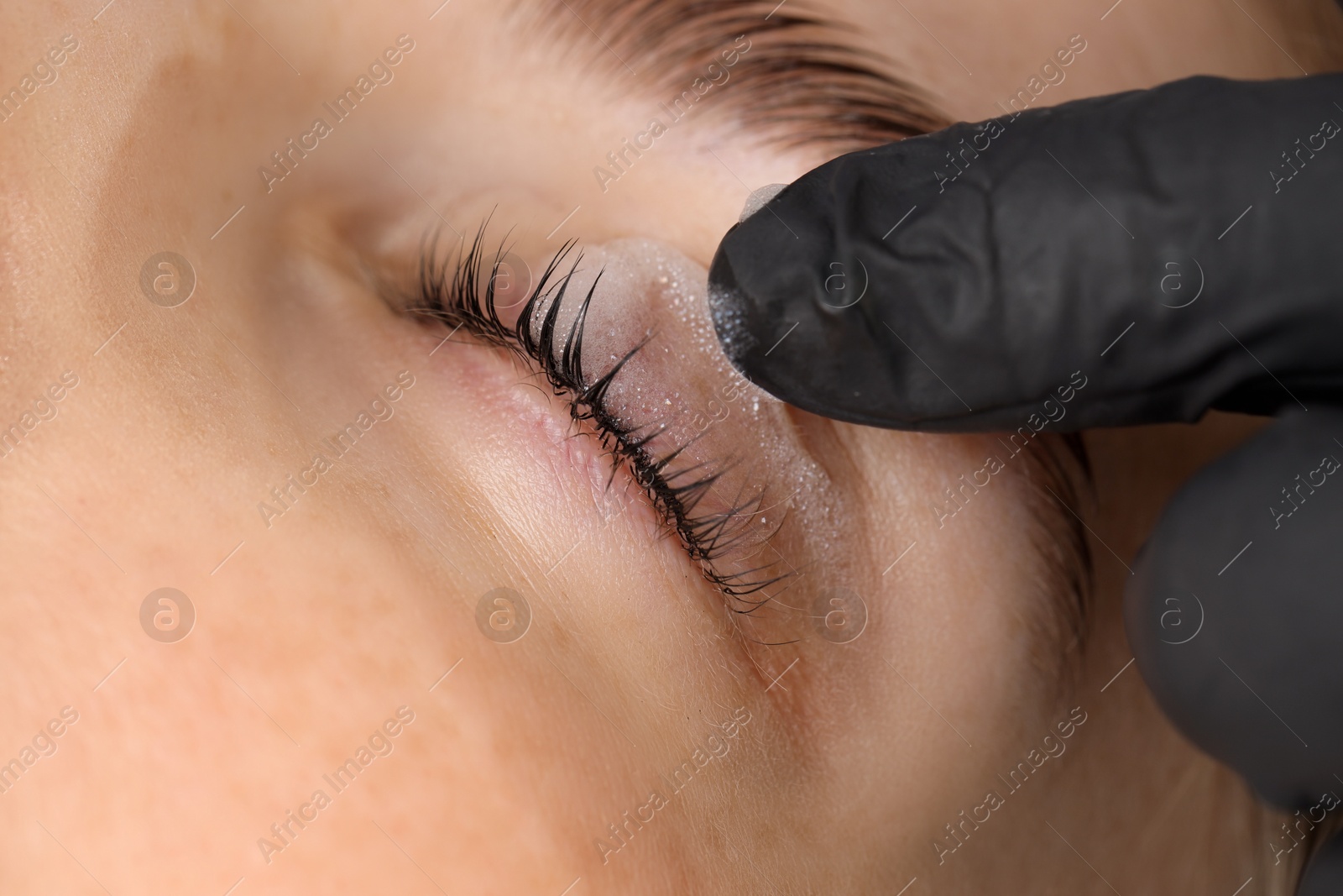 Photo of Esthetician cleaning woman's lashes after lamination procedure, closeup