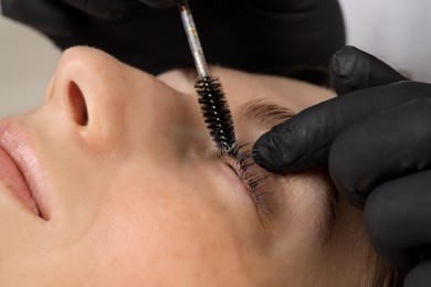 Photo of Esthetician brushing woman's lashes after lamination procedure, closeup