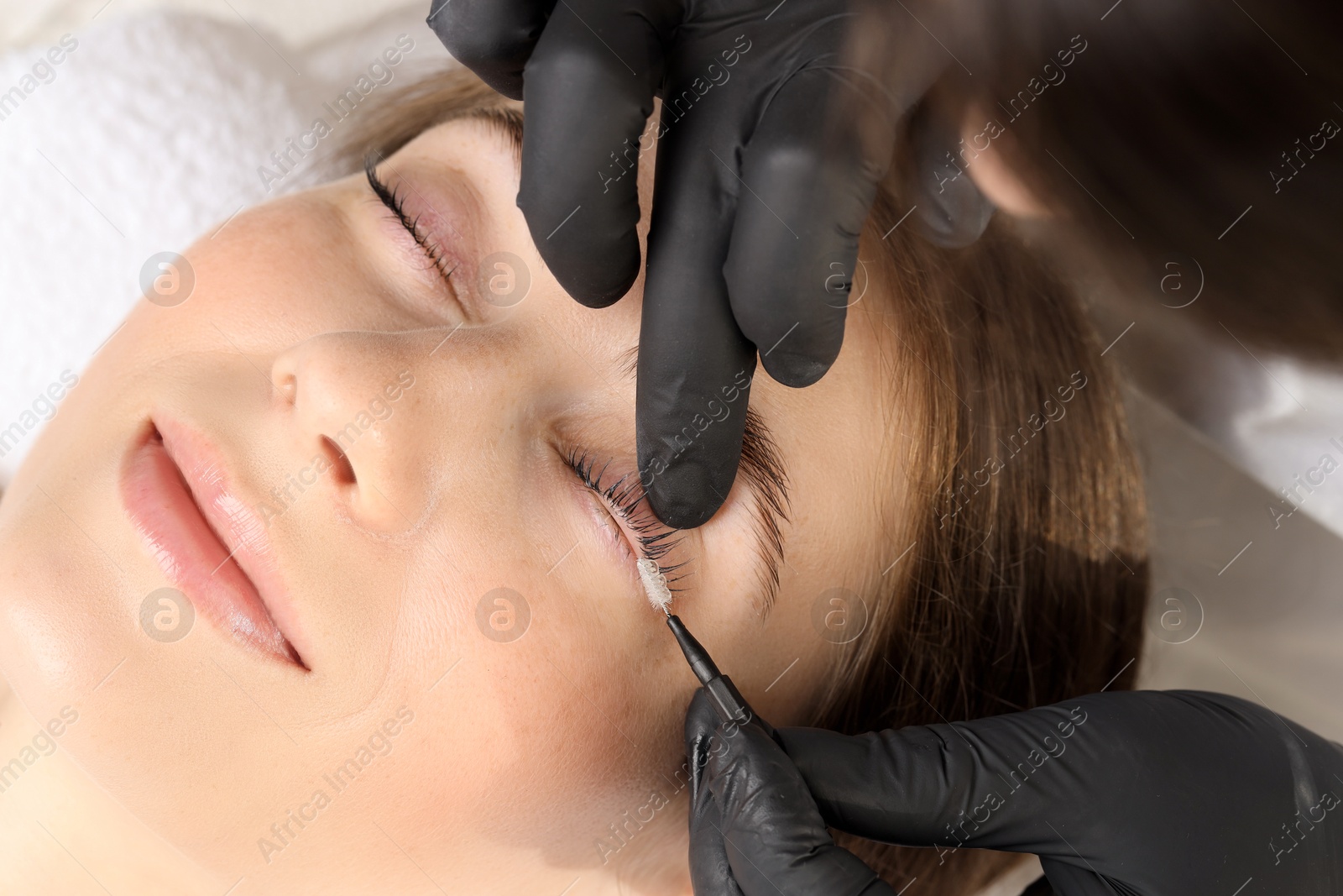 Photo of Esthetician brushing woman's lashes after lamination procedure, closeup