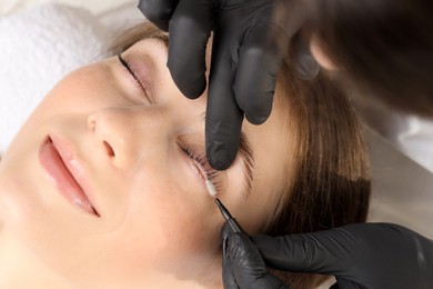 Photo of Esthetician brushing woman's lashes after lamination procedure, closeup