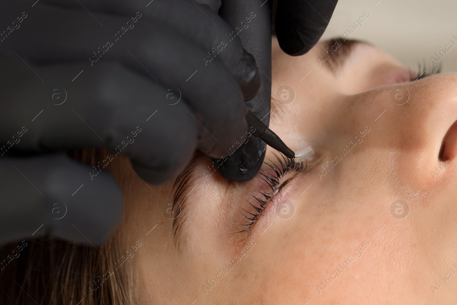 Photo of Esthetician brushing woman's lashes after lamination procedure, closeup