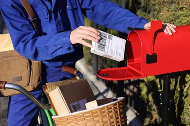 Postman with bicycle putting parcel into mail box outdoors, closeup