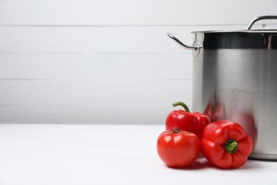 Photo of Stainless steel pot and vegetables on white table, space for text