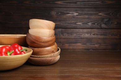 Photo of Bowls with peppers on wooden table, space for text. Cooking utensils