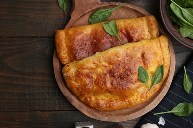 Photo of Tasty calzones with basil on wooden table, top view