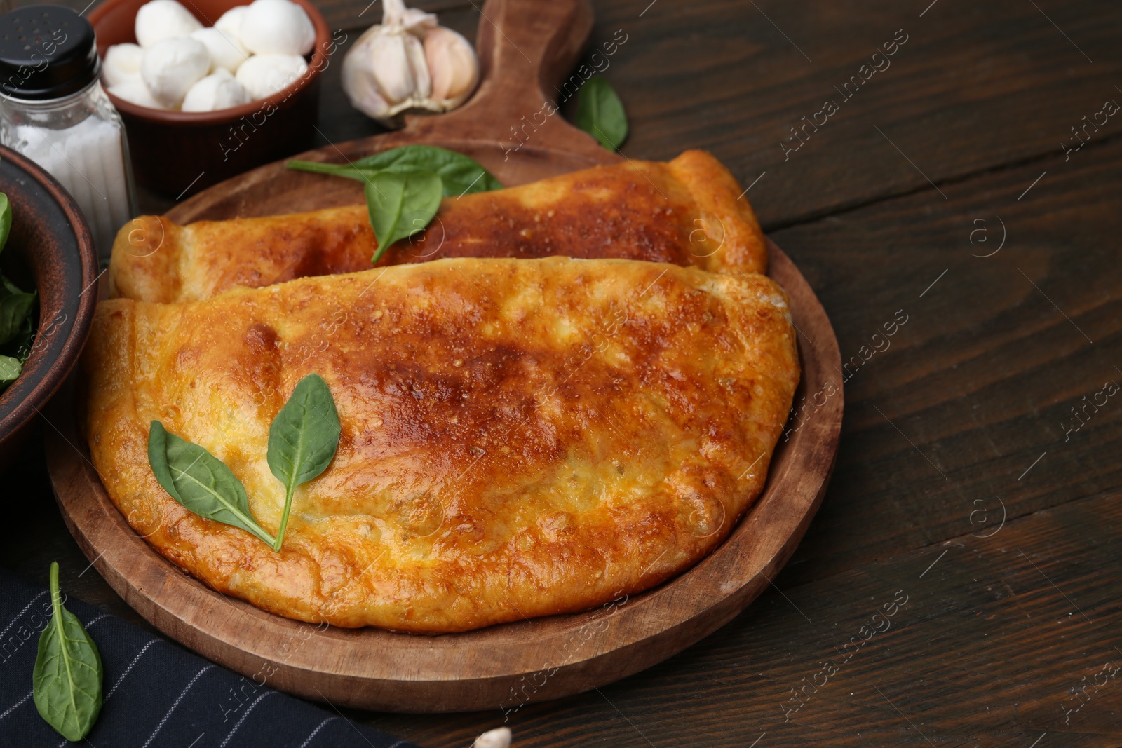 Photo of Tasty calzones with basil, mozzarella cheese and garlic on wooden table, closeup. Space for text