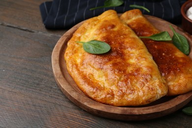 Photo of Tasty calzones with basil on wooden table, closeup. Space for text