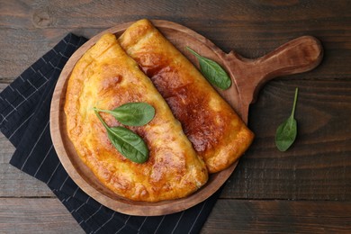 Photo of Tasty calzones with basil on wooden table, top view