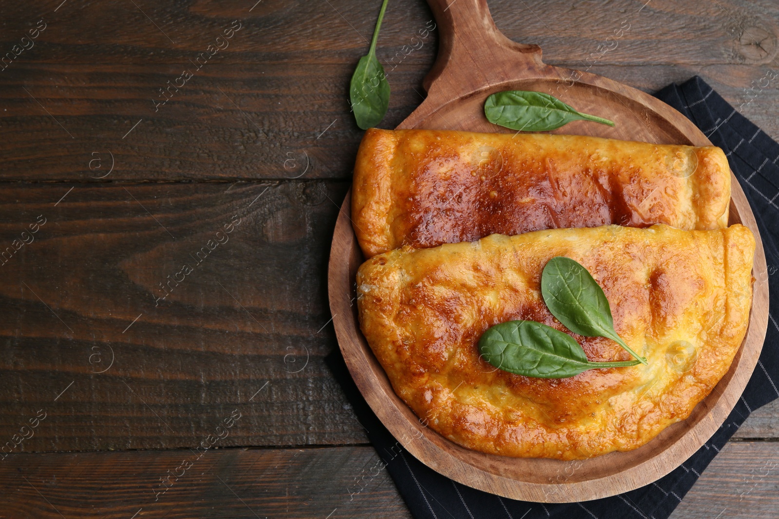 Photo of Tasty calzones with basil on wooden table, top view. Space for text