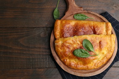 Photo of Tasty calzones with basil on wooden table, top view. Space for text