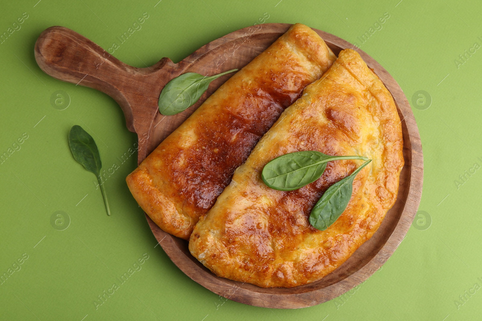 Photo of Tasty calzones with basil on green background, top view