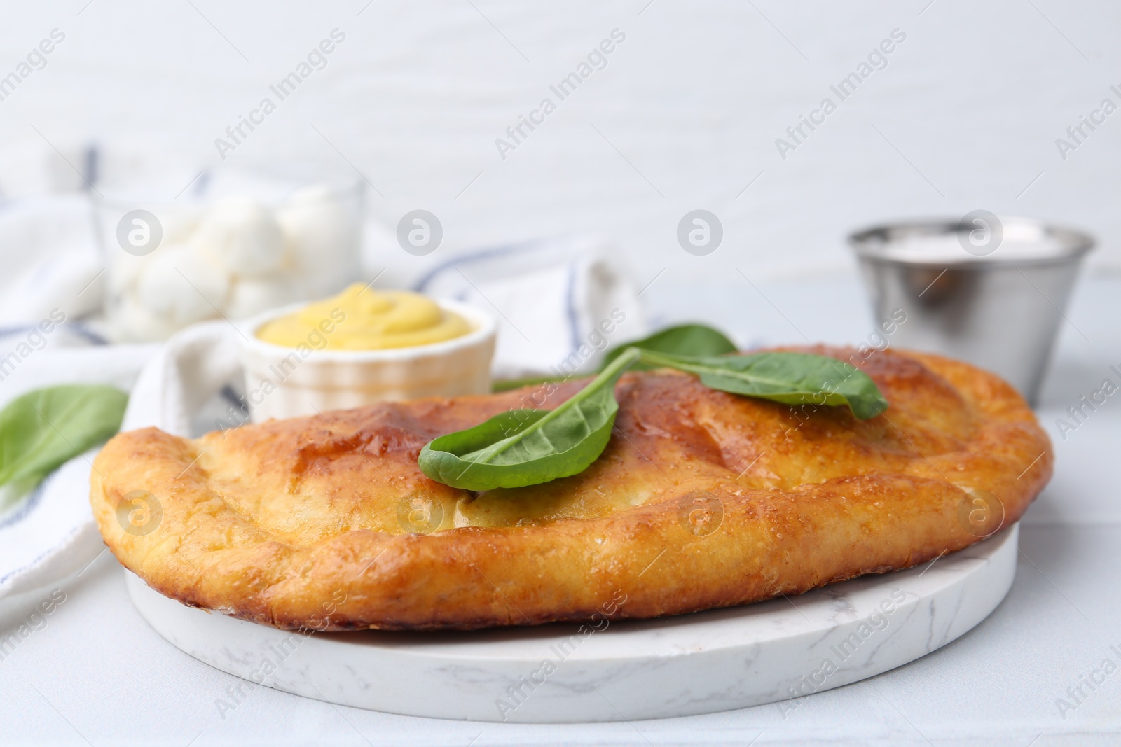 Photo of Tasty calzone with basil and sauce on white table, closeup