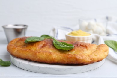 Photo of Tasty calzone with basil and sauce on white table, closeup