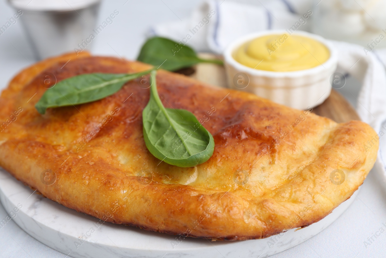 Photo of Tasty calzone with basil and sauce on white table, closeup