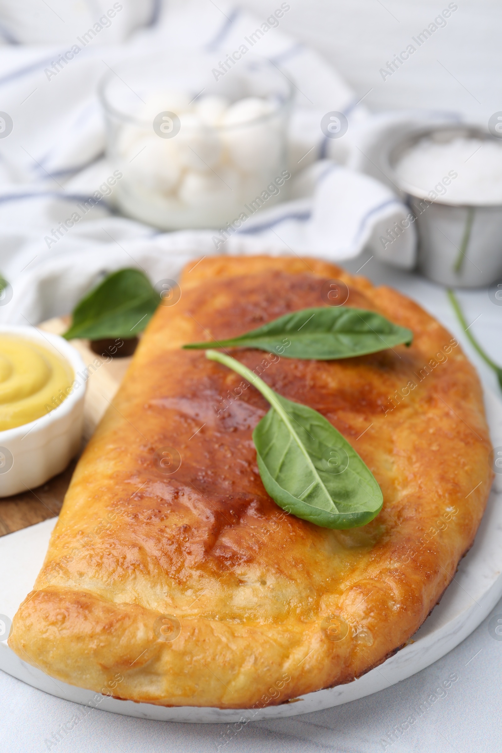 Photo of Tasty calzone with basil and sauce on white table, closeup