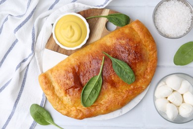 Photo of Tasty calzone with basil served on white tiled table, flat lay