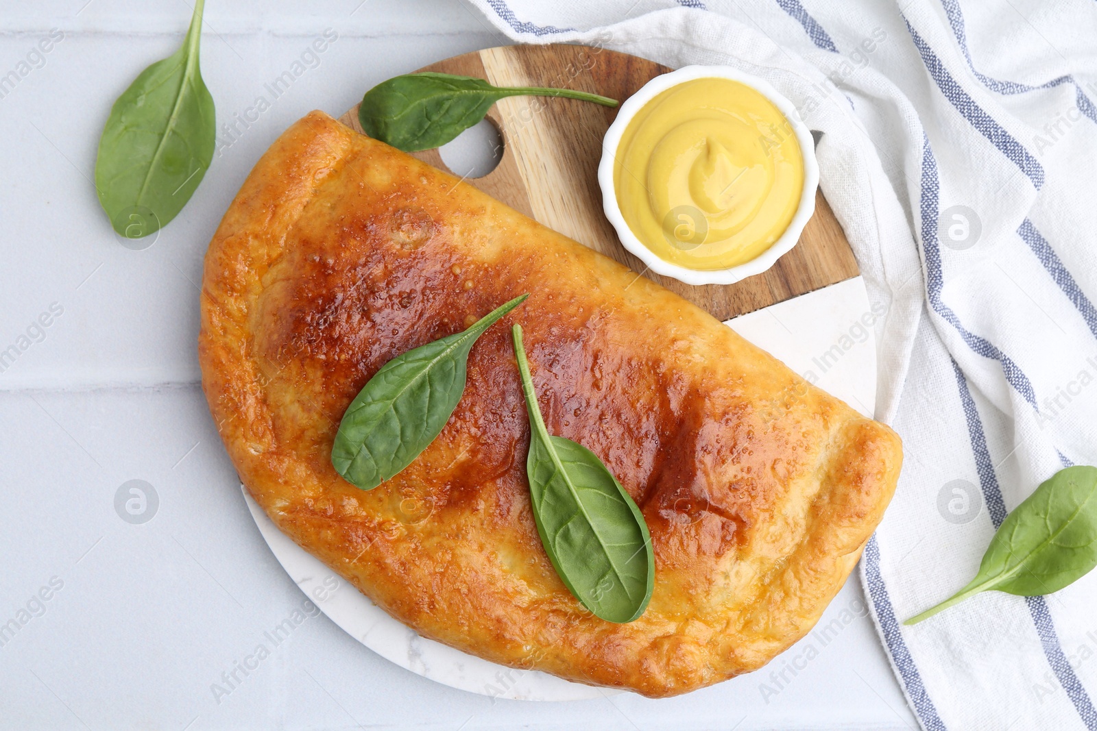 Photo of Tasty calzone with basil and sauce on white table, top view