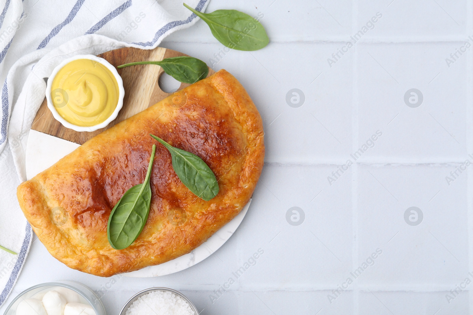 Photo of Tasty calzone with basil served on white tiled table, flat lay