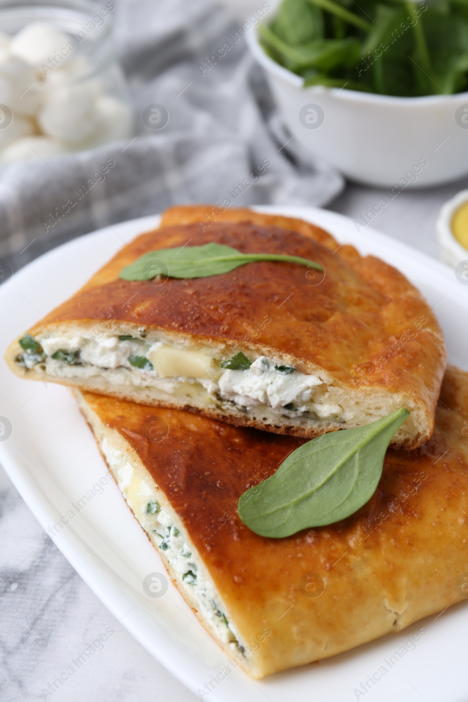 Photo of Pieces of tasty calzone with cheese and basil on white marble table, closeup