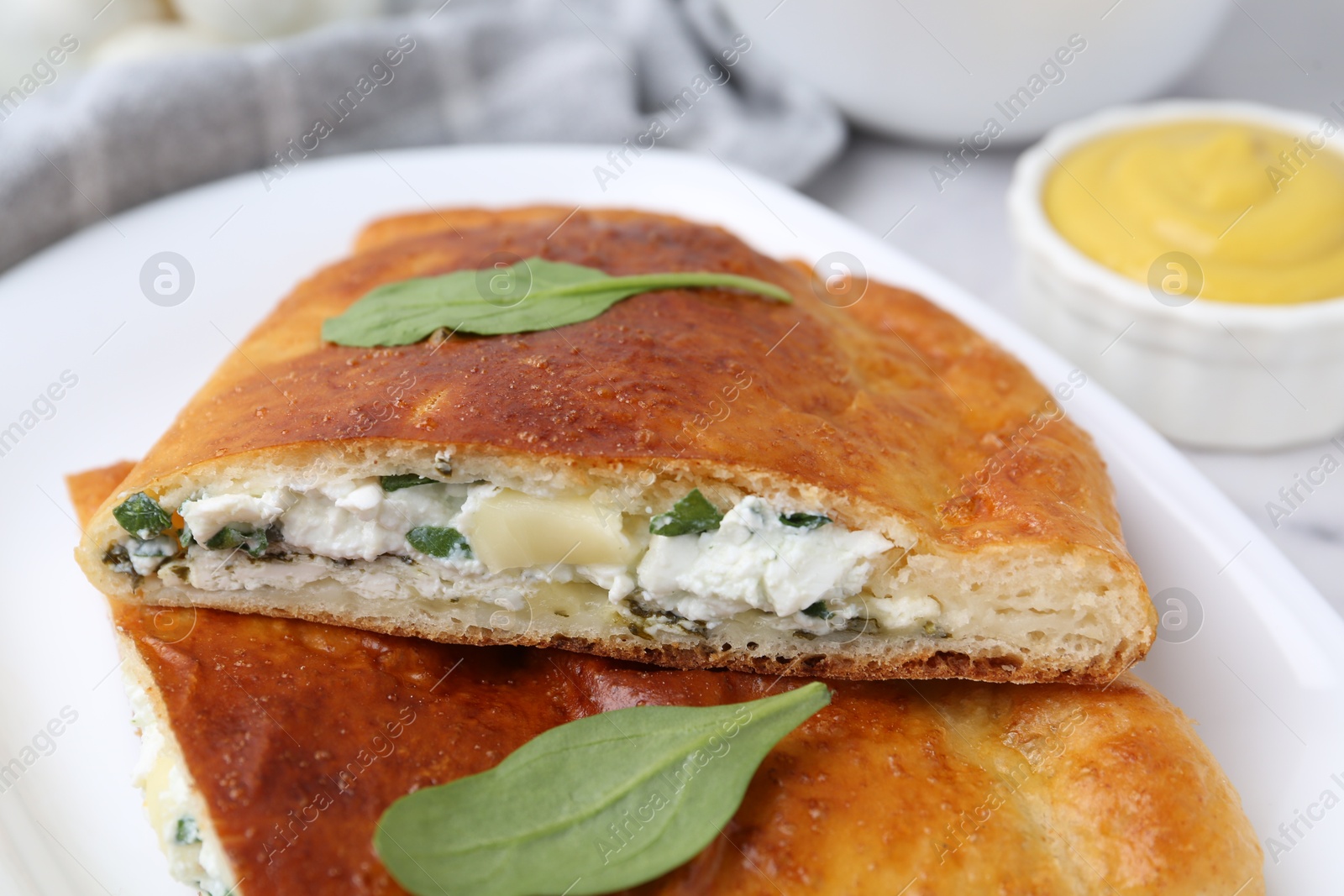 Photo of Pieces of tasty calzone with basil, cheese and sauce on table, closeup