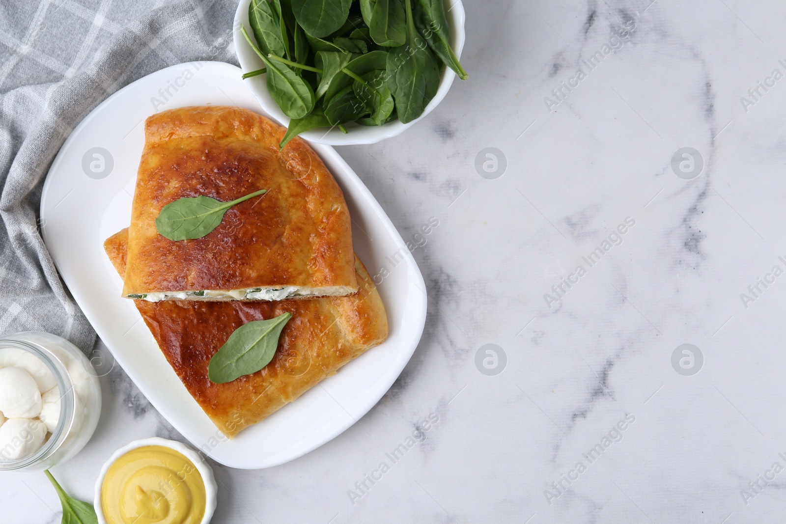 Photo of Pieces of tasty calzone with basil, mozzarella cheese and sauce on white marble table, flat lay. Space for text