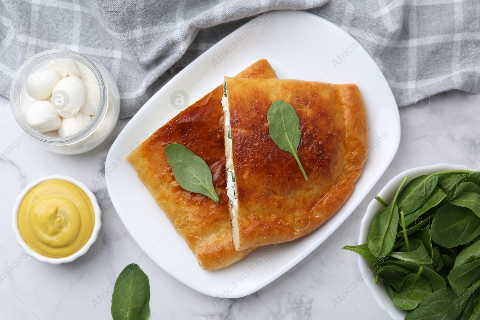 Photo of Pieces of tasty calzone with basil, mozzarella cheese and sauce on white marble table, flat lay