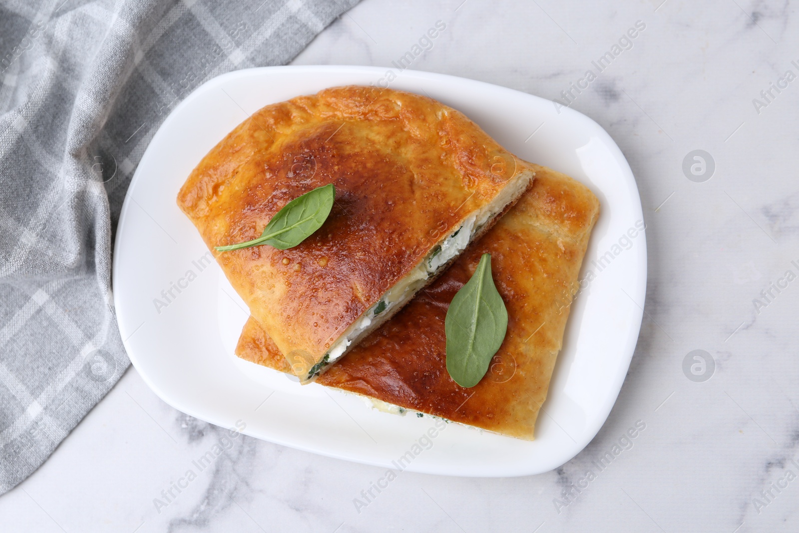 Photo of Pieces of tasty calzone with cheese and basil on white marble table, top view