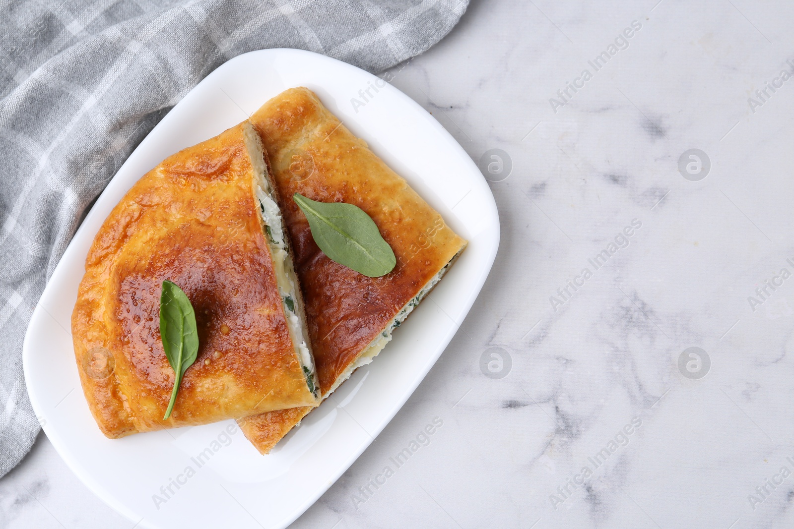 Photo of Pieces of tasty calzone with cheese and basil on white marble table, top view. Space for text