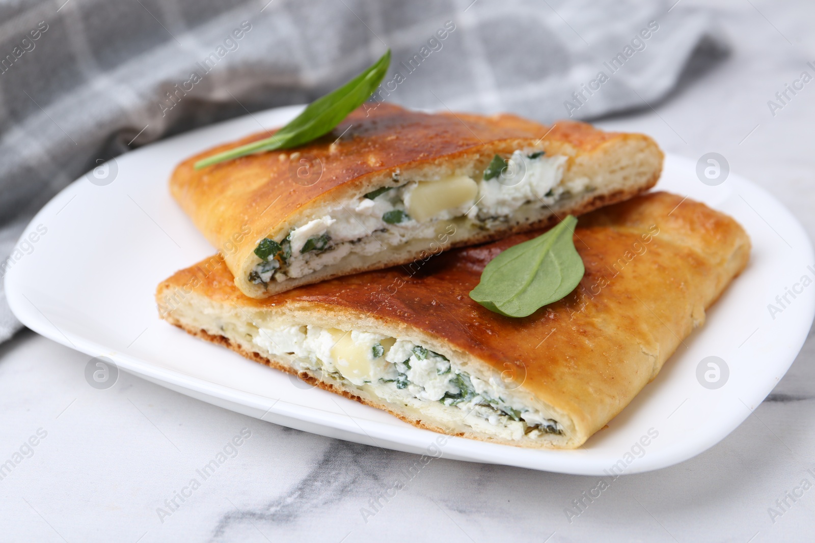 Photo of Pieces of tasty calzone with cheese and basil on white marble table, closeup