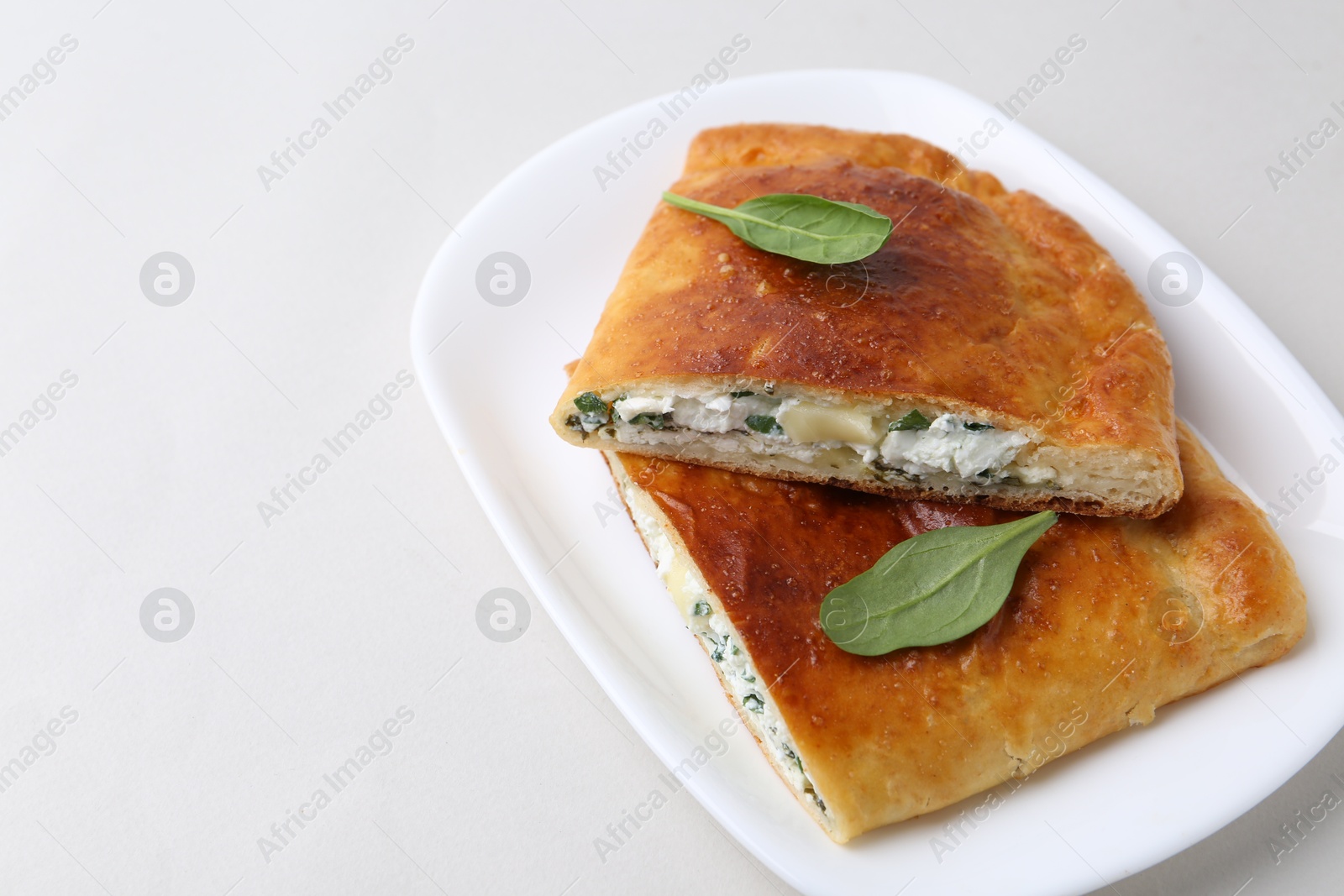 Photo of Pieces of tasty calzone with cheese and basil on white background, closeup. Space for text