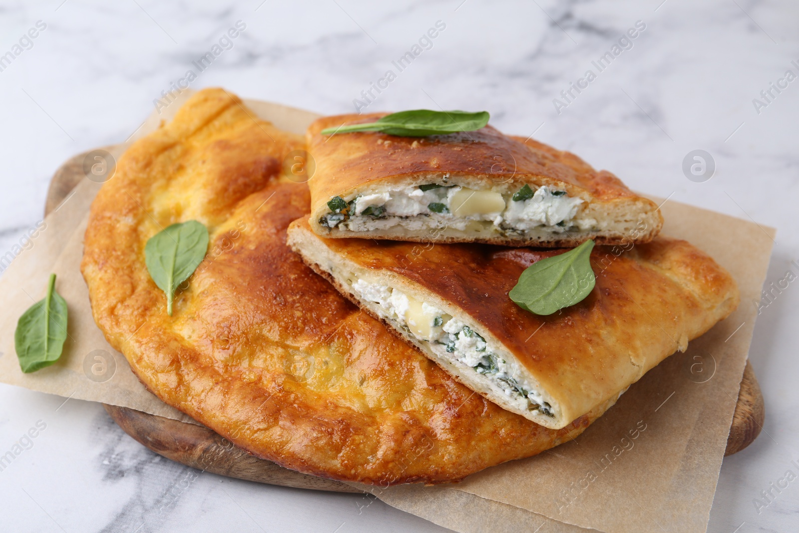 Photo of Tasty calzones with cheese and basil on white marble table, closeup