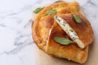 Photo of Tasty calzones with cheese and basil on white marble table, closeup. Space for text