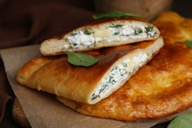 Photo of Tasty calzones with cheese and basil on table, closeup