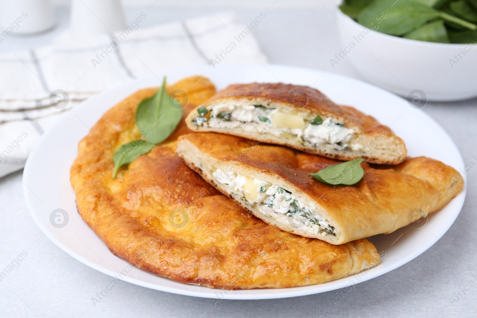 Photo of Tasty calzones with cheese and basil on light grey table, closeup