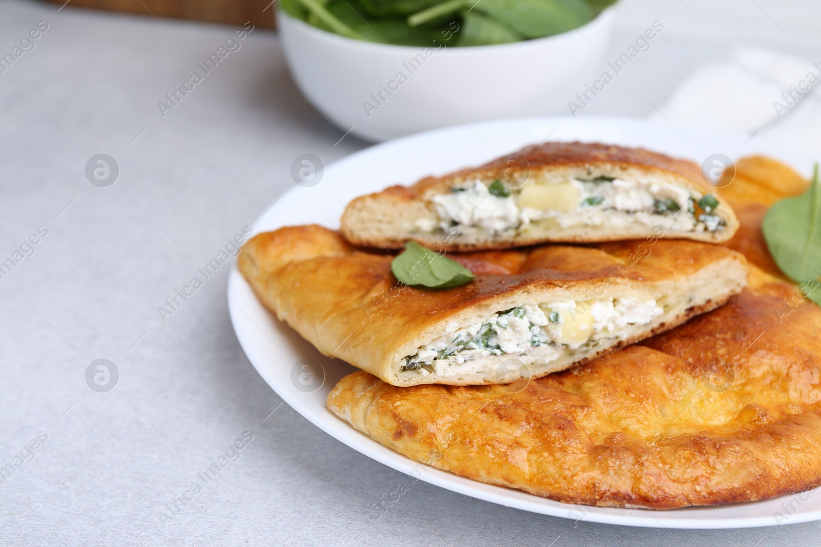 Photo of Tasty calzones with cheese and basil on light grey table, closeup. Space for text