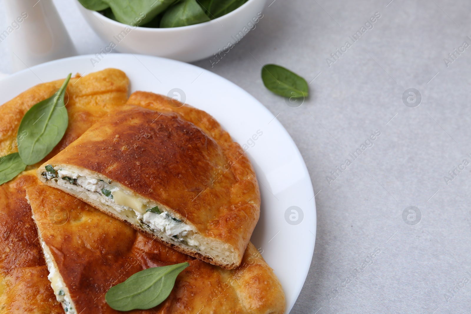 Photo of Tasty calzones with cheese and basil on light grey table, closeup. Space for text