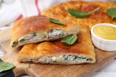 Photo of Pieces of tasty calzone with basil, cheese and sauce on table, closeup